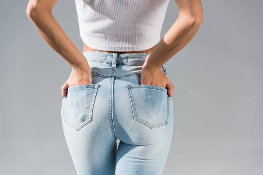 Cropped view of young woman in jeans with hands in pockets isolated on grey